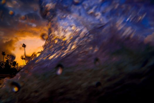 Dramatic sunset over the exotic beach, with palms and sea wave close up, low angle view.