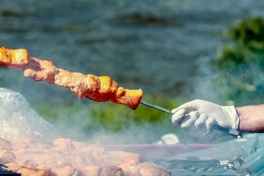 Hand in glove holds a skewer with a kebab made of fish