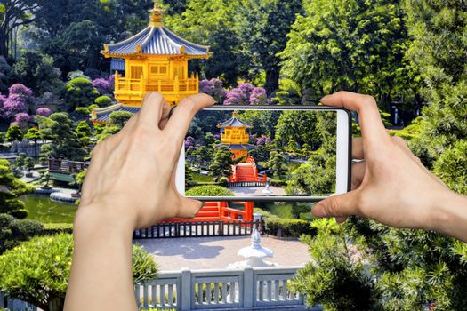 Girl taking pictures on mobile smart phone in Front View The Golden Pavilion Temple in Nan Lian Garden