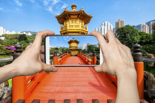 Girl taking pictures on mobile smart phone in Front View The Golden Pavilion Temple in Nan Lian Garden