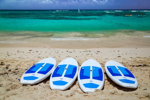 Surfboards on the beach. Surfing board on the beach with ocean view nobody. surfboards abandoned on an empty sandy beach with waves in distance. Amazing tropical beach with surfboards against azure ocean, white sand and blue sky. Caribbean wild nature scenery near the beach in Punta Cana.