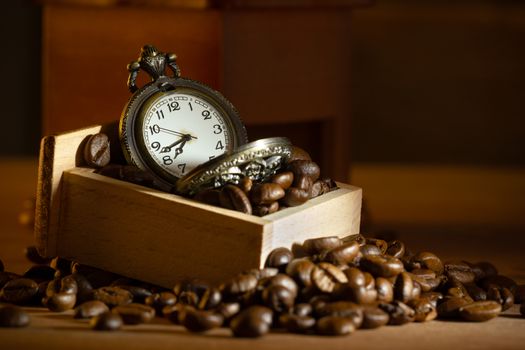 Coffee bean and pocket watch in manual grinder on table. Closeup and copy space. Concept of coffee time in morning.