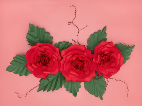 Red paper roses and tiny white flowers with dried veins on salmon pink background.
