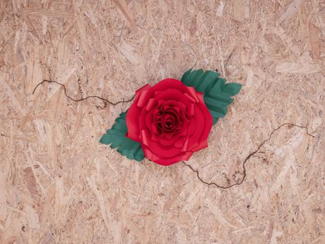 A beautiful hand-crafted paper crimson red rose with thorny veins on vintage wooden board background.