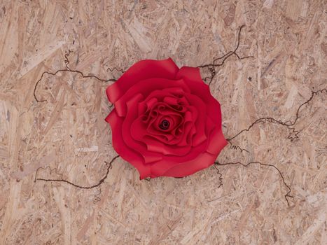 Beautiful hand-crafted paper crismson rose on thorny veins. Wooden board background.