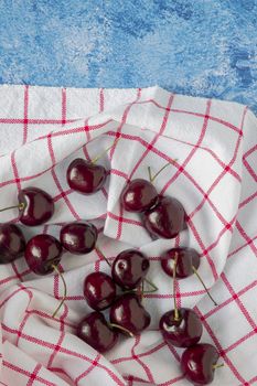 Red cherries on a table with red and white checkerboard cloth. Blue paint background.