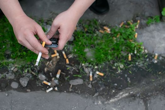 hands of a Smoking man who holds a mobile phone while sitting on the street against the background of cigarette butts, garbage and trash scattered on the ground