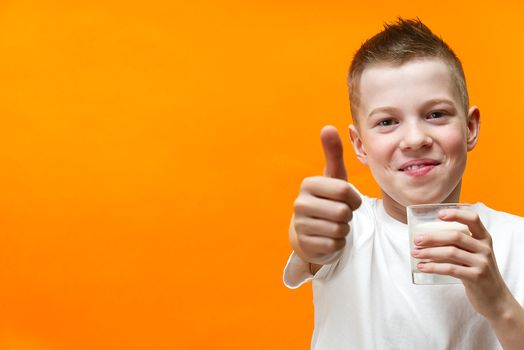 handsome boy drinks milk and shows ok gesture with thumb on orange background