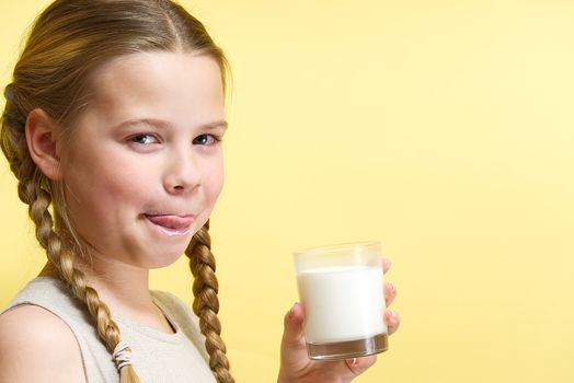 girl with pigtails and milk mustache drinks milk on yellow background