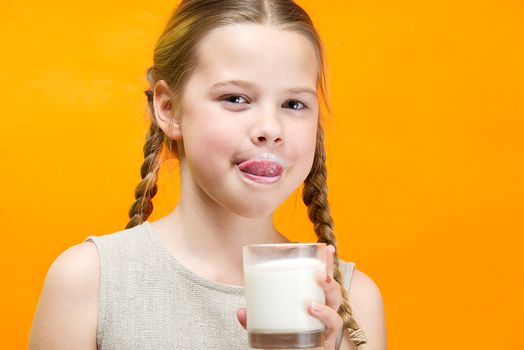 girl with pigtails and milk mustache drinks milk on orange background