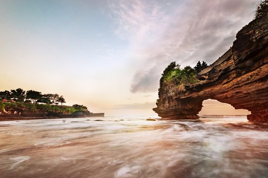 Sunset near famous tourist landmark of Bali island - Tanah Lot & Batu Bolong temple. Long exposure effect, Bali Indonesia. Tropical nature landscape of Indonesia, Bali.