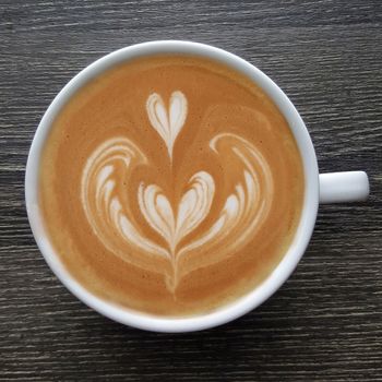 Top view of a mug of latte art coffee on timber background.