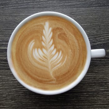 Top view of a mug of latte art coffee on timber background.