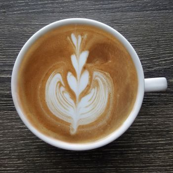 Top view of a mug of latte art coffee on timber background.