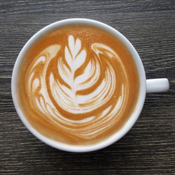 Top view of a mug of latte art coffee on timber background.