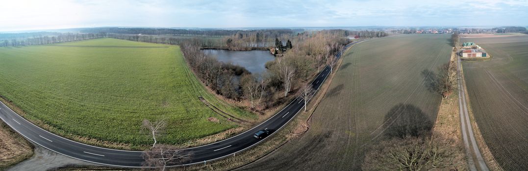 Composite panorama of aerial photographs and aerial photos of a straight road next to a pond and a field, abstract effect due to distortion due to the large overall angle of the photograph, drone shot
