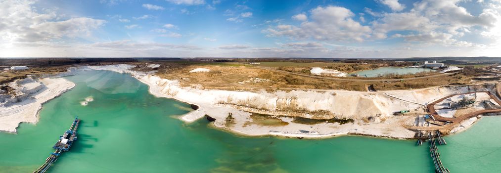 Composite panorama of aerial photographs and aerial photos of a wet mining operation for white quartz sand with a green and blue dugout lake and a large suction dredger, made with drone