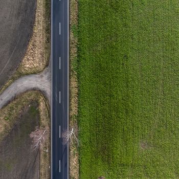 Aerial view of an asphalted country road in Germany with a farmland on the left and a green meadow on the right side. Abstract impression due to vertical angle of view. Made with drone