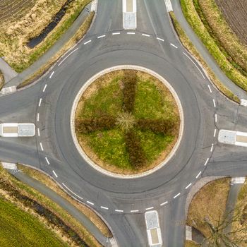 Aerial view of a small roundabout at the intersection of two asphalted gray country roads in the north of Germany, abstract