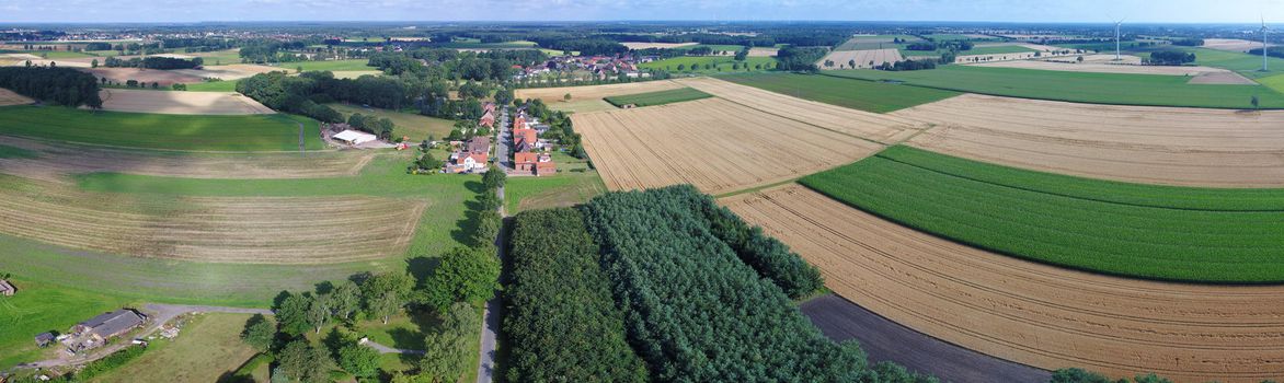 Aerial view of fields, meadows and forests with a street in the middle and a small village in the background, drone landscape