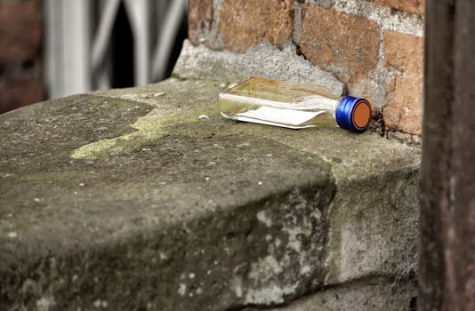 Empty hip flask for brandy in a dirty corner of a house on a concrete slab in front of old red bricks, alcohol , concept