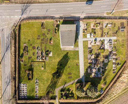 Aerial photo of the small cemetery of a village with an asphalted country road at the upper edge of the aerial photo. Made with drone