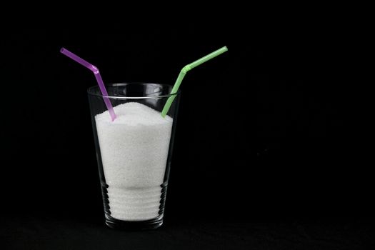 Clear glass full of sugar on black background with two straws with copy space