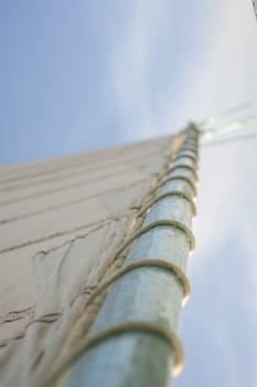 Abstract view of wooden sailing boat mast with shallow depth of field selective focus showing rigging on blue sky background