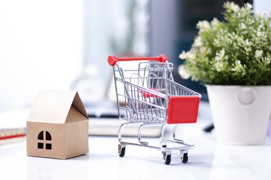 shopping online concept :Shopping Cart onthe box with paper home mock up. Shooping online delivery at home.Work desk blur background.Copyspace for text. nobody.Online Delivery. 