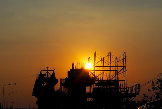 Sunset on the road. Silhouette on the pillar and steel structures that is under the construction. Background of sky is orange.