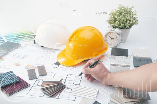 Hand of Engineer write material on the planning paper. Sample of Mable stone. Materials Construction. House planning on the Interior Desk. Safety Helmet on the desk. 