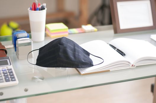 Black mask on the work table to protect virus and dust. Empty notebook for text on the desk.