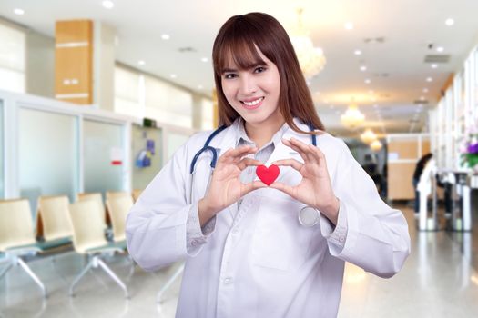 Young Asian woman doctor holding a red heart, standing on hospital background. healthy care concept