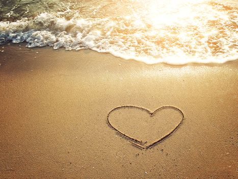 Hearts drawn on the sand of a beach with white bubble waves at sunset time