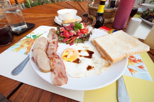 English breakfast with fried eggs, bacon, sausages, toasts and fresh salad