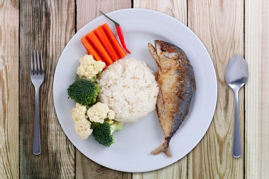 Mackerel fried with chilli sauce Thai style food. Healthy food. Mackerel fish with carrot and broccoli on white flat plate on wooden table from top view