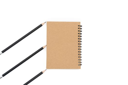 This brown book is placed in the center of the picture and three black pencils on the left side of the picture diagonally and on a white background.