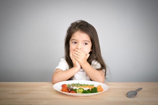 Nutrition & healthy eating habits for kids concept. Children do not like to eat vegetables. Little cute kid half race girl refuse to eat healthy vegetables.