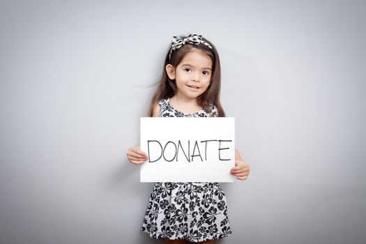 little cute girl with handwriting text donations on white paper. helping, giving , donate and donation concept