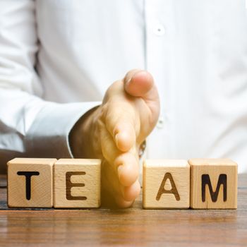 A man shares with his hand cubes with the inscription team. Dividing the collective into two parts or disbanding the team. Lack of leadership qualities and poor quality of business management.