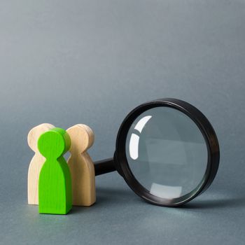 Three wooden human figure stands near a magnifying glass on a gray background. The concept of the search for people and workers. Search for vacancies and work. Human resources, management.