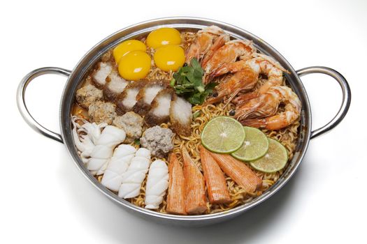 Pot of spicy instant noodles isolated on white background. Topping with eggs, lemon, pork , crispy pork, sausage , shrimp, squid, crab and coriander