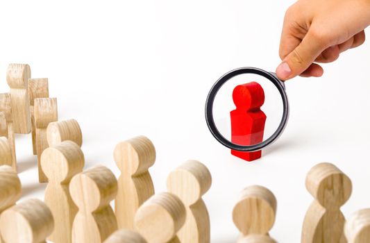 A magnifying glass looks at a red figurine of a man near a crowd. Leader, leadership and initiator of action. work or business organization. team building. Idol and example to follow. Distrust