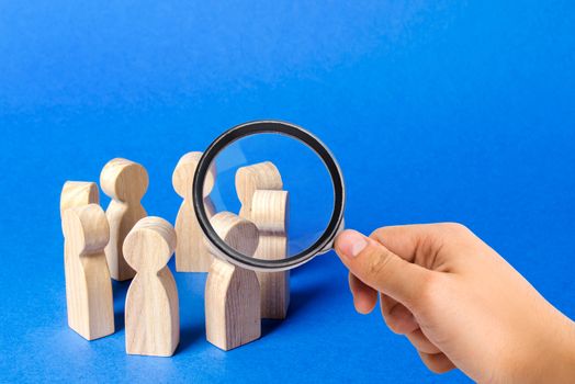 A magnifying glass looks at a people figurines stand in a circle. discussion, cooperation. Meeting at work, negotiating a plan of action. teamwork. Employees briefing. Organization of work processes