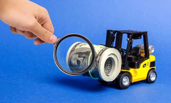 A magnifying glass looks at a forklift truck carries a bundle of dollars. Attracting direct investment in business and production, improving economic performance. capitalism. Export of capital