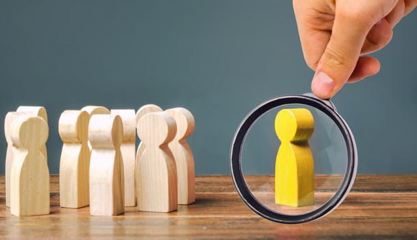 A magnifying glass looks at a yellow figurine of a man stands aside from the crowd of people. Asociality, sociopathy. Rejected from society, lonely. Development of leadership and social qualities.