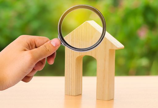 A magnifying glass looks at a wooden figure of a house with a large doorway. Home, Affordable housing, residential building. concept of buying or selling real estate, rent, investment and construction