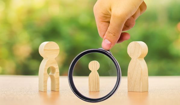 A magnifying glass looks at a child's figure stands between father and mother. The child chooses which parent to live with after their divorce. Guardianship over child. interest of child