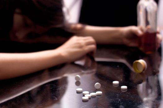 a drug addict not conscious on the table with several pill spilled on table near bottle of alcohol.