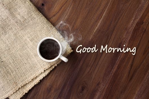 Cup of hot coffee with smoke on wooden table top view with word good morning. coffee background with copy space